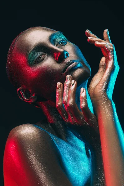 Art beauty portrait. Perfect fashion model girl with black painted skin and sparkling glitter makeup posing in color neon light. Makeup and cosmetics. Jewelry.
