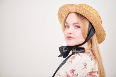 Hasır şapkalı tatlı sarışın kız ve yaz bluzu beyaz arka planda gülümsüyor. Pembe renkli açık renk makyaj. Bahar ve yaz güzelliği. Moda. Boşluğu kopyala.  