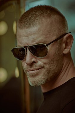 Erkek tarzı. Kısa saçlı ve kıllı, modaya uygun güneş gözlüğü takan yakışıklı ve vahşi bir adamın portresi. Erkekler için optik. 
