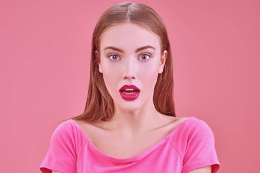 Parlak makyajlı güzel bir kız büyük gözleriyle kameraya bakar ve şaşırır. Pembe arka planda bir portre. Güzellik, makyaj ve kozmetik konsepti.