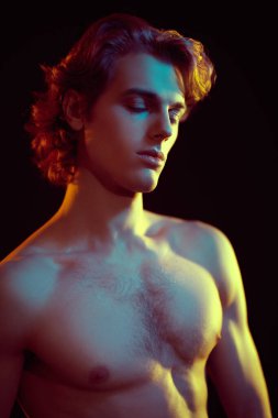 Güzel sarı saçlı, siyah arka planda karışık renkli ışık şeklinde poz veren yakışıklı bir atletik adamın sanat portresi. Erkek güzelliği. Spor ve sağlıklı yaşam tarzı.