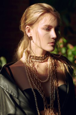 Siyah iç çamaşırlı, siyah deri ceketli, altın sarısı ve inci takılı sarışın bir kadının portresi. Moda fotoğrafı. Lüks yaşam tarzı. 