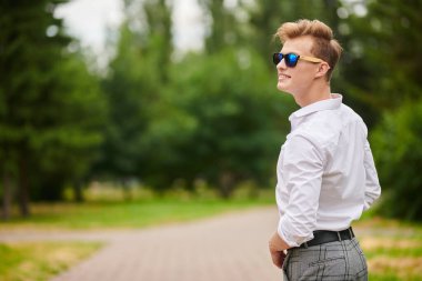 Yakışıklı genç adam parkta yürüyor ve gülümsüyor. Yaz modası. Yaz tatili ve tatil.