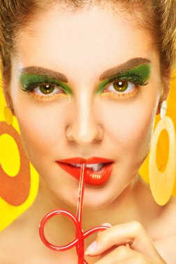 Güzellik ve poster tarzı. Parlak makyajlı, sarı arka planda soda içen çekici bir kızın yakın plan portresi. Makyaj ve kozmetik.