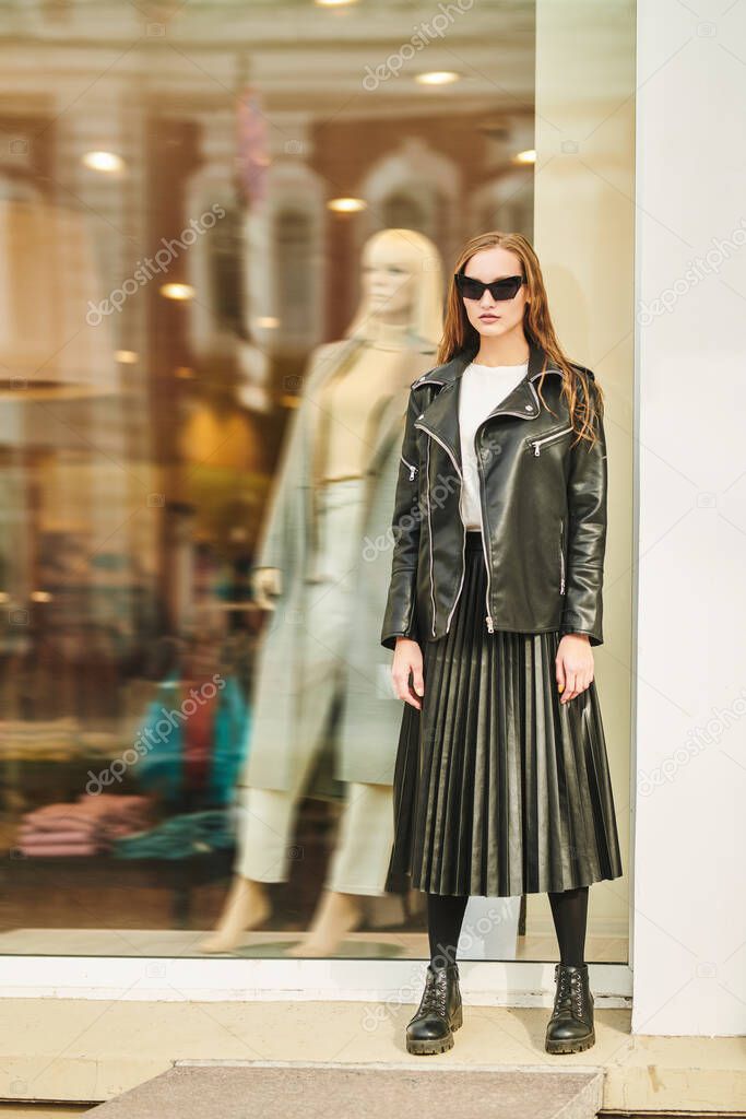 Fashionable lady in black clothes poses against the background of a fashion store window in a city street.