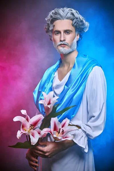 Roman and Greek mythology, Christianity and religion. Art image of God. Divine man with a beard and curly hair holds lily flower on a blue background.