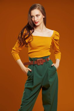 Koyu turuncu arka planda renkli giysiler içinde güzel, modaya uygun genç bir kadının portresi. Moda fotoğrafı. Giysilerdeki parlak renkler. 