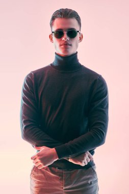 Koyu renk kazaklı ve modern siyah güneş gözlüklü yakışıklı bir genç. Erkek aksesuarları, optikler. Stüdyo resmi.