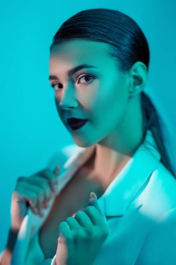 Zarif ceketli esmer kadın renkli akuamarin ışıklarıyla poz veriyor. Güzellik portresi. Makyaj ve kozmetik.