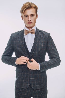 Sarı saçlı yakışıklı genç adam şık bir klasik takım elbise ve beyaz lüks dairelerde papyon takıyor. Erkek güzelliği, moda. 