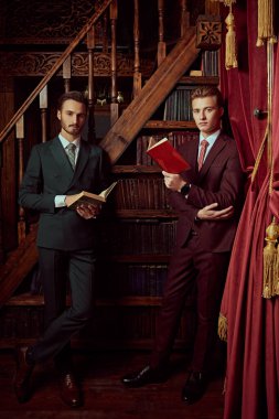 Klasik takım elbiseli iki yakışıklı gencin portresi erkekler kulübündeki lüks dairelerde vakit geçiriyor. Erkek güzelliği, moda.