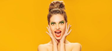 Renkli makyajlı, sarı arka planda ifadesiyle poz veren çekici ve etkileyici bir kızın portresi. Makyaj ve makyaj malzemeleri. İnsani duygular. Boşluğu kopyala. 