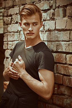 Tuğla duvarın yanında siyah tişörtle poz veren çekici genç adam modeli. Erkek stili, güzellik. Moda fotoğrafı.. 