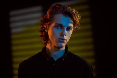 Koyu arkaplanda dalgalı sarı saçlı, parlak ve gölgeli yakışıklı bir gencin portresi. Erkeklerin güzelliği. 