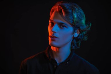 Siyah arka planda dalgalı sarı saçlı, karışık renkli ışık saçan yakışıklı bir gencin portresi. Erkek güzelliği. Boşluğu kopyala.