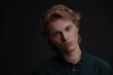 Kameraya bakan dalgalı sarı saçlı yakışıklı bir gencin portresi. Kopyalama alanı olan siyah arkaplan. Erkek güzelliği. Boşluğu kopyala.