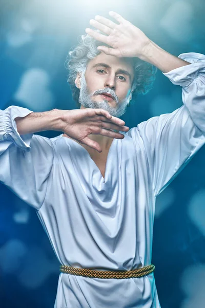 Divine man with a gray beard and curly  hair in a white tunic on a blue background with hearts. Art image of God. Roman and Greek mythology, Christianity and religion.