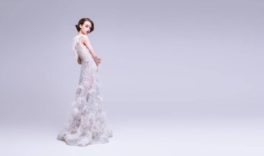 Düğün modası. Stüdyoda gri arka planda poz veren beyaz elbiseli, çarpıcı genç bir kadının tam boy portresi. Uzayı kopyala Moda fotoğrafı.. 