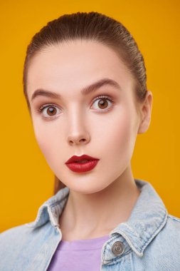 Sarı arka planda kırmızı dudakları ve doğal makyajı olan güzel bir genç kızın portresi. Güzellik, makyaj, kozmetik.