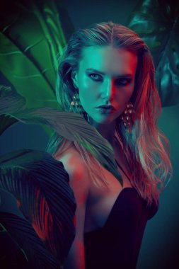 Islak saçlı güzel ateşli kadın tropikal bitkilerin arasında duruyor. Güzellik, moda ve kozmetik konsepti. Tropikal ülkelerde tatil.