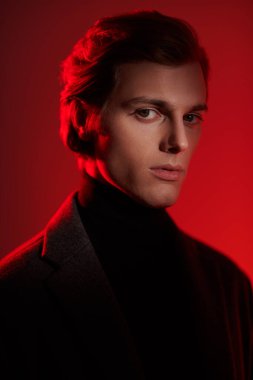 Stüdyoda kırmızı ışıkta poz veren zarif elbiseli yakışıklı sarışın bir adamın portresi. Erkeklerin güzelliği. 