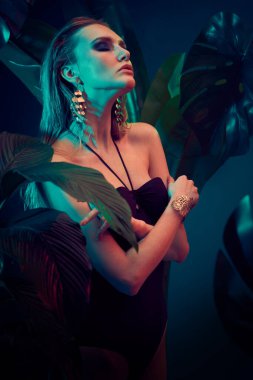 Islak saçlı güzel ateşli kadın tropikal bitkilerin arasında duruyor. Güzellik, moda ve kozmetik konsepti. Tropikal ülkelerde tatil.