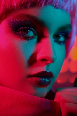 Parlak parlak makyajlı ve karışık renkli neon ışıklı pembe saçlı göz kamaştırıcı bir manken kız portresi. Makyaj malzemesi ve saç stili. 
