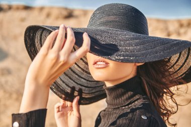 Çölde geniş kenarlı şapkalı zarif esmer bir kadının yakın plan portresi. Moda fotoğrafı. Yaz tatili.
