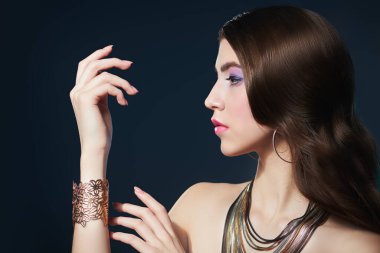 Koyu bir arka planda uzun dalgalı saçlarla poz veren muhteşem bir genç kadının portresi. Güzellik, moda ve mücevher.. 