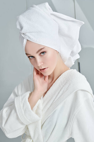 Портрет красивой молодой женщины в белом халате и полотенце вокруг волос после душа. Красота, уход за телом, спа.