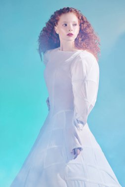 Sanat ve moda. Saf kırmızı kıvırcık saçlı, beyaz bir elbise içinde poz veren zarif bir manken kızı portresi. Stüdyo çekimi. 
