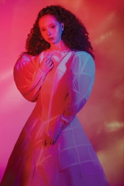 Moda sanatı. Beyaz bir sanat elbisesi içinde poz veren gür kırmızı kıvırcık saçlı sofistike bir kadın modelin portresi. Kırmızı renkli, karışık bir stüdyo portresi.