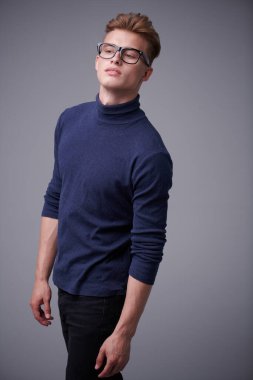 Sarı saçlı, gözlüklü yakışıklı genç adam gri arka planda poz veriyor. Erkekler için optik. Erkek güzeli.. 