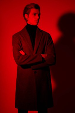 Stüdyoda kırmızı ışıkta poz veren zarif elbiseli yakışıklı bir gencin portresi. Erkek stili.