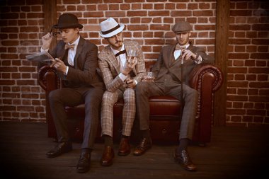 Zarif giyimli üç yakışıklı adam kulübün içinde çatı katında vakit geçiriyor. İş adamları kulübü. Erkek modası.