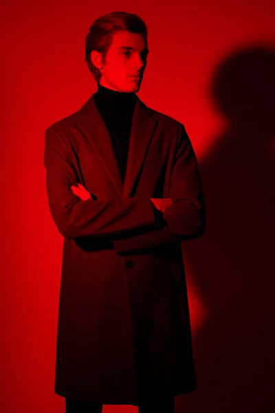 Portrait of a handsome young man in elegant clothes posing at studio in red light. Men\'s style.
