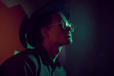 Sigara içen yakışıklı ve etrafı dumanla çevrili genç bir adam. Stüdyo portresi.