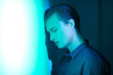 Yakışıklı genç adam, üzgün ve yalnız duruyor, karanlık ışıkta duvara yaslanıyor. Duygular ve duygular. Boşluğu kopyala. 