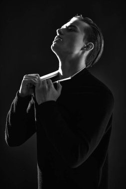 Siyah-beyaz bir portre. Stüdyoda karanlık ışıkta ifade ile poz veren cesur bir genç. Erkek güzelliği. Siyah arkaplan. 
