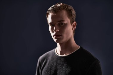 Stüdyoda karanlık ışıkta poz veren sarışın yakışıklı bir adamın portresi. Erkek güzelliği. Kopyalama alanı olan siyah arkaplan. 