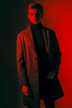 Stüdyoda kırmızı ışıkta şık kıyafetler giymiş zarif bir erkek modelin portresi. Moda fotoğrafı..