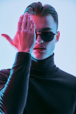 Modern güneş gözlüklü yakışıklı genç adam bir gözünü eliyle kapatıyor. Erkek aksesuarları, optikler. Stüdyo resmi. 