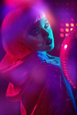 Gece partisi tarzı. Parlak makyajlı ve gece kulübünün neon ışıklarında poz veren pembe saçlı modern bir kız portresi. Disko biçimi. 
