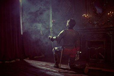 Zırhlı asil şövalye diz çöktü ve kaledeki ışığa bakarak elinde gülü tuttu. Aşk.. 