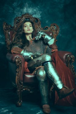 Full length portrait of a medieval queen in knightly armor sitting on a throne on a vintage background. History of the Middle Ages. clipart