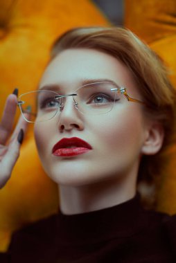 Sarı bir kanepede uzanmış zarif gözlüklü çekici bir bayan. Güzellik, moda. Optik biçimi.