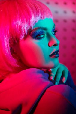 Parlak makyajlı ve pembe peruklu güzel bir kız neon ışıklarla poz veriyor. DJ kız gece partisinde. Disko biçimi. 