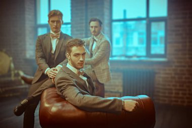 Zarif görünümlü üç yakışıklı, dairelerin içinde poz veriyor. İş adamları kulübü. Erkek modası.