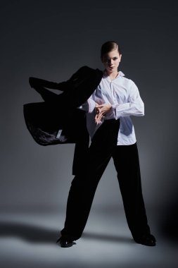 Moda konsepti. Siyah kadife takım elbise ve gri arka planda beyaz gömlekle hareket eden zarif genç bir kadının tam boy portresi.. 