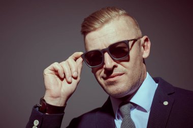 Başarılı, saygıdeğer, takım elbiseli ve gri arka planda güneş gözlüğü takan olgun bir adam. İş adamı portresi. Portreyi kapat.